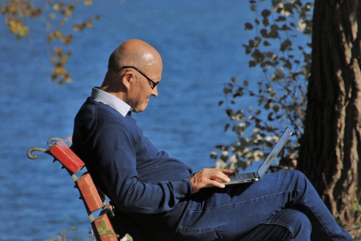 Mężczyzna z laptopem siedzący na ławce nad jeziorem