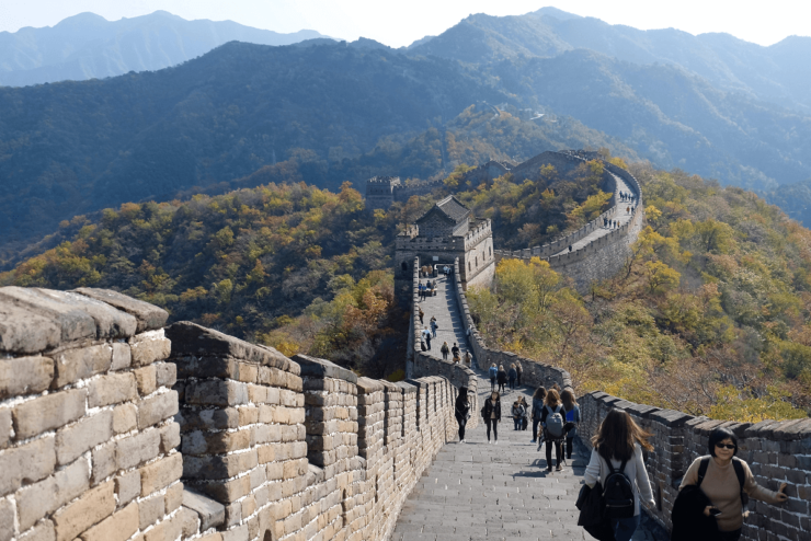 Zdjęcie ilustrujące spacer po Wielkim Murze Chińskim przedstawiające turystów spacerujących po Murze, w tle zalesione wzgórza.