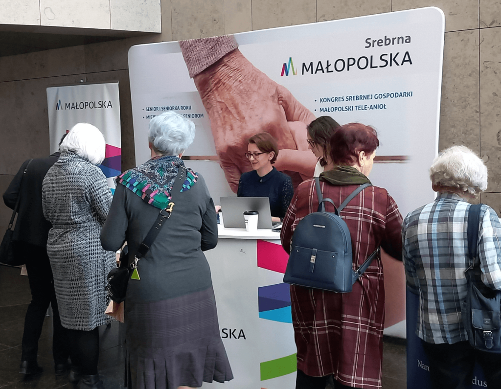 Osoby przy stoisku Srebrna Małopolska podczas prezentacji portalu Senioralna Małopolska.